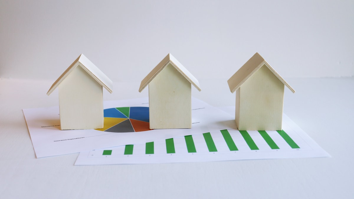 Maquettes de maisons en bois posées sur des graphiques financiers, pour un achat destiné à la location